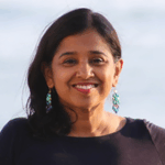 An Indian woman with long dark hair and dangly turquoise earrings smiles