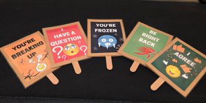 A photo of cards made to use on Zoom. From left, they read “you’re breaking up” with an emoji surrounded by cracks; “I have a question” with a confused emoji and question marks;, “you’re frozen” with a blue, ice-covered emoji; “be right back” with a red figure running to the right of the sign; and “I agree” with a smiley emoji and thumbs-up emoji.