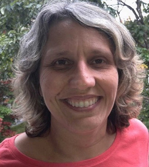 A white woman with wavy light-colored hair is smiling.