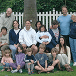 A large family sits beneath a tree.