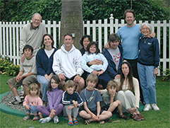 A large family sits beneath a tree. 