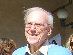 An older white man with white hair and glasses smiles in a close-up image. 