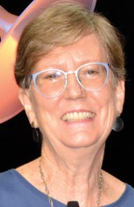 A white woman with short light hair and glasses smiles. 
