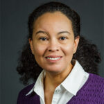 Knashawn Morales photo. Hair to her shoulders, white blouse with collar, under a purple sweater. She is smiling.