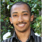 Photo of Lester Mackey, Tree in background. He is smiling, has a mustache and is wearing a striped shirt.