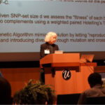 A white woman with short hair stands behind a presentation screen at a lectern.