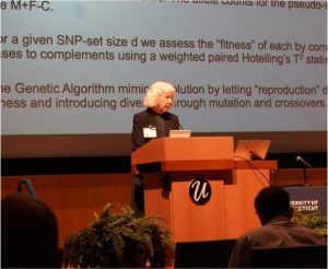 A white woman with short hair stands behind a presentation screen at a lectern.