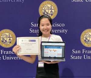 Lana Huynh, an Asian woman, stands in front of a purple backgound that has the San Francisco State University logo repeating across it. She is smiling and holding a laptop displaying her research and a certificate. 