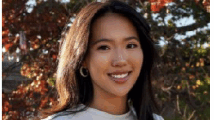 Lucy Tu in front of fall leaves, shoulder length dark hair, smile, hoop earrings.