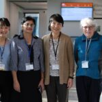 Six people pose and smile. Left to right, there is are four Asian women, a white woman, and a south Asian man.