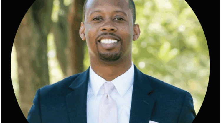 Derek Curtis II, wearing a suit and tie. Smiling