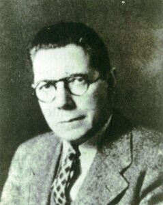 Portrait of Raymond Pearl, a man with short dark hair who is wearing glasses and a suit and tie