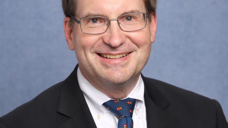 Photo of Mark Hansen. Suit and tie, smiling