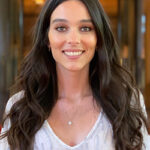 A white woman with long dark hair and a white shirt smiles
