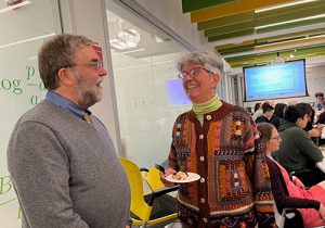 A white man with a beard and gray hair and glasses talks to a white woman with short gray hair and glasses.
