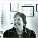 Black and white photo of Barbara Bailar, short hair, smile, in an office.