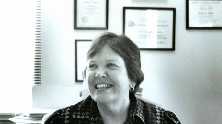 Black and white photo of Barbara Bailar, short hair, smile, in an office.