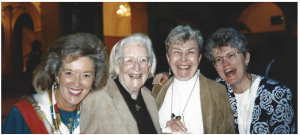 Katherine Wallman, blonde hair, bright scarf, all women are close together and have their arms around each other Margaret Martin, glasses, Mary Grace, white turtle neck sweater, Kovar, and Virginia DeWolf short hair, big smiles 