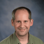 A white man wearing a green shirt smiles