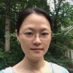 An Asian woman with her hair pulled back wearing clear glasses 
