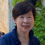 An Asian woman with short dark hear wearing a dark blue collared shirt smiles
