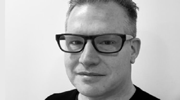 Black and white headshot of Zink. Glasses, short hair