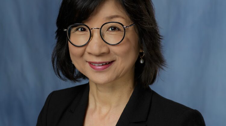 A photo of Ji-Hyun Lee with short black hair, glasses, and a dark suit jacket, smiling at the camera