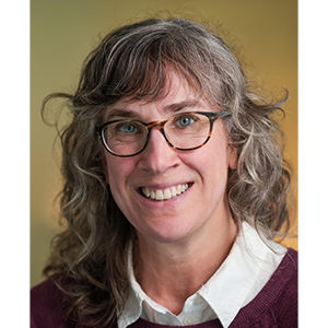 Portrait of Elizabeth Colantuoni, a smiling white woman with shoulder-length gray hair and round glasses