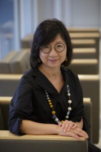 Portrait of Ji-Hyun Lee, sitting at table, looking at camera; she wears glasses and has chin-length hair