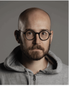 Portrait of Van Dam, bald, round dark glasses, beard, mustache