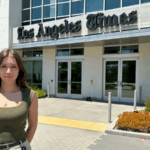 A white womam with long dark hair wearing a tank top stands in front of the LA Times building.