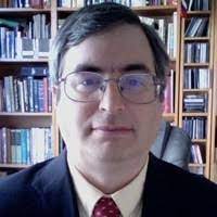 A white man wearing glasses with short dark hair and a suit and tie