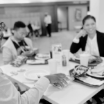 Raphiel Murden (black man) at the 2023 ASA StatFest-sitting at a table with paper plate in front of him-big smile on his face