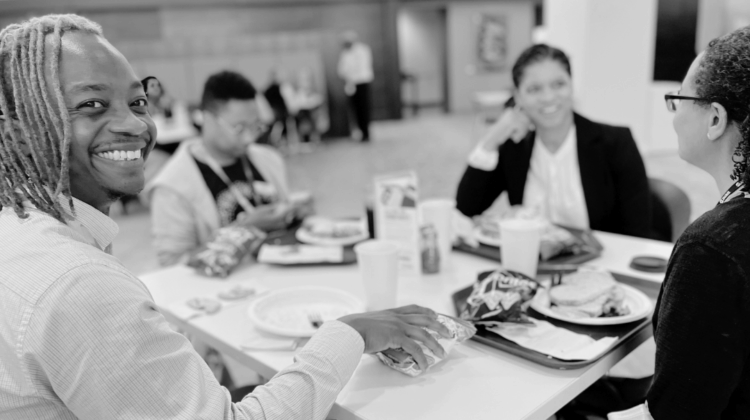 Raphiel Murden (black man) at the 2023 ASA StatFest-sitting at a table with paper plate in front of him-big smile on his face