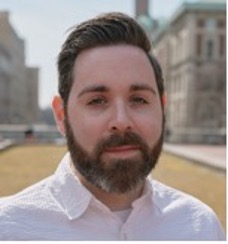 A white man with short dark hair and a dark beard in a white dress shirt