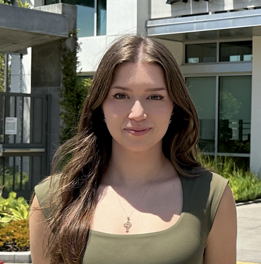 A white womam with long dark hair wearing a tank top stands in front of the LA Times building.