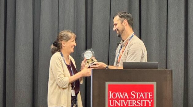 A man presents a woman with an award. The man is standing behind a podium that reads "Iowa State University." 
