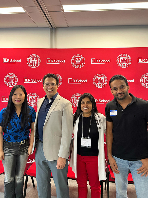 Four people stand in front of a red background
