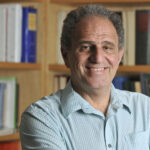A white man with gray hair smiles in front of a bookcase