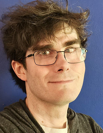 A white man with rectangular glasses and short dark hair smiles slightly