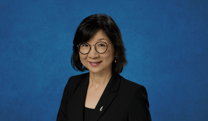 A photo of Ji-Hyun Lee with short black hair, glasses, and a dark suit jacket, smiling at the camera