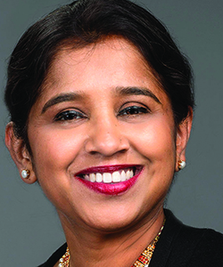 An Indian woman with short dark hair, sparkly earrings, and bright pink lipstick smiles