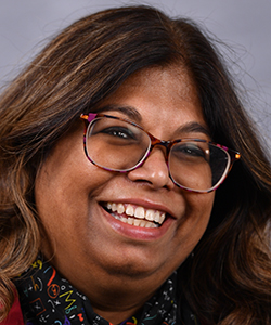 A southeast Asian woman with long brown hair, glasses, and a scarf smiles