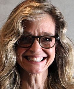 A blonde white woman with long wavy hair and glasses smiles