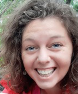 A white woman with curly hair and light eyes smiles