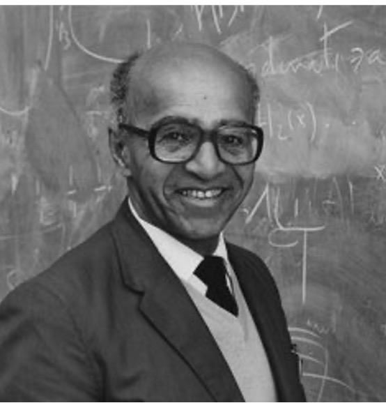 A photo of David Blackwell, smiling while wearing large-framed glasses and a suit jacket with sweater and tie.