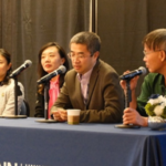 Panel discussion, four individuals, sitting in front of a table with microphones in front of them