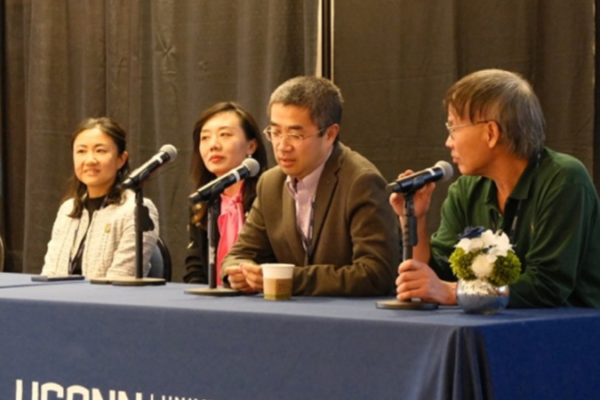 Panel discussion, four individuals, sitting in front of a table with microphones in front of them