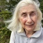Gray hair, blowing in wind. Wearing a high-collar zippered top.