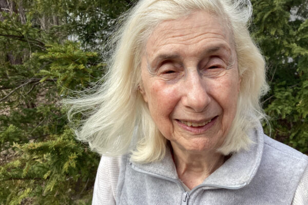 Gray hair, blowing in wind. Wearing a high-collar zippered top.